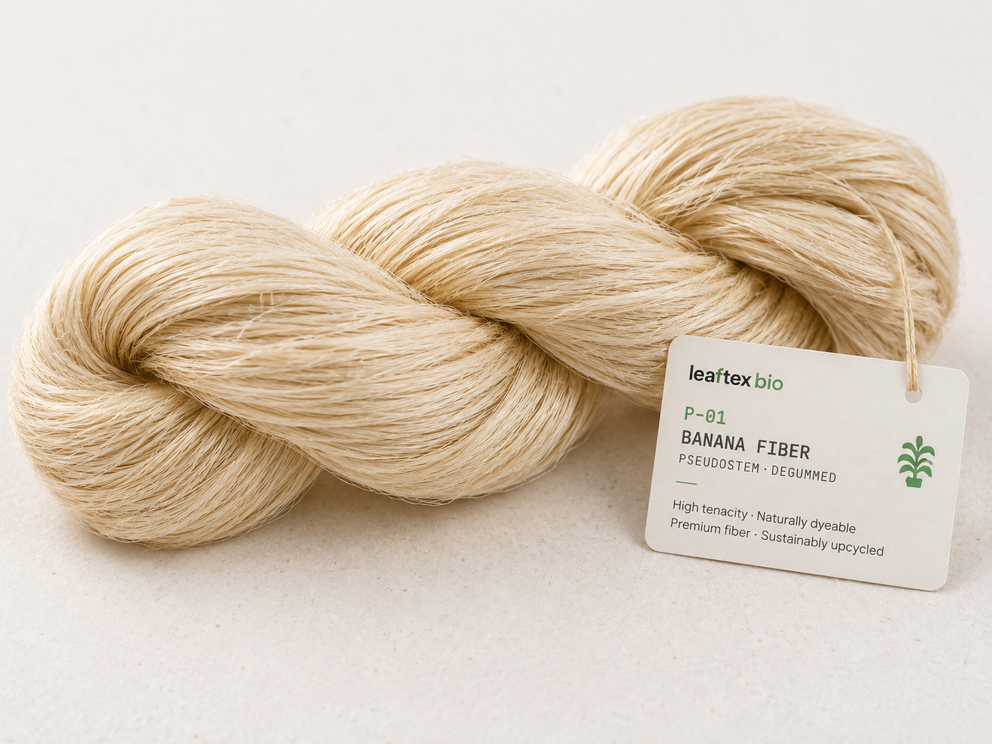 Hero macro of a hank of banana fiber yarn — natural cream tones. Twisted skein on pale stone surface.
